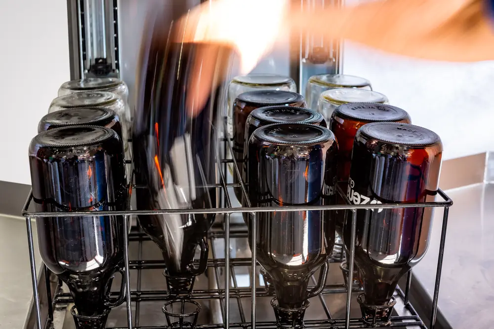 Bouteilles ambrées placées goulot en bas sur les buses du panier du lave-bouteilles