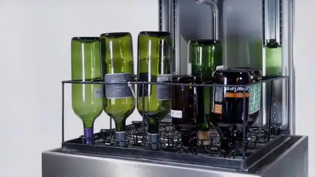 Green wine bottles in the basket of a commercial bottle washer